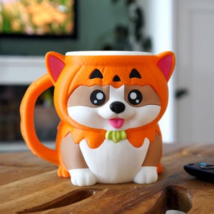 May include: A ceramic mug shaped like a cartoon Shiba Inu dog. The mug is orange, brown, white, and pink, with a green bow tie. The mug has a handle and is sitting on a wooden surface.