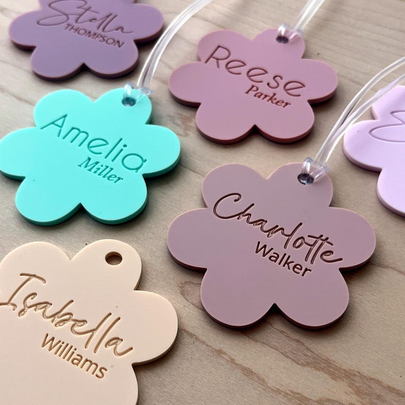 May include: Five colorful flower-shaped luggage tags with names and last names printed on them. The tags are made of a soft, flexible material and have a clear plastic loop for attaching to luggage.