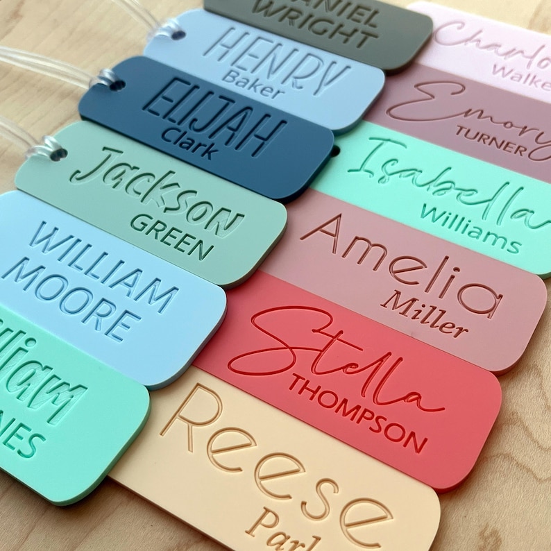 May include: A set of ten personalized luggage tags with various names and last names printed on them. The tags are made of colorful plastic and have a rectangular shape. The names include:  'Daniel Wright', 'Henry Baker', 'Elijah Clark', 'Jackson Green', 'William Moore', 'Isabella Williams', 'Amelia Miller', 'Stella Thompson', 'Reese Parker', and 'Emory Turner'.