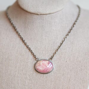 May include: A silver chain necklace with a pink oval pendant