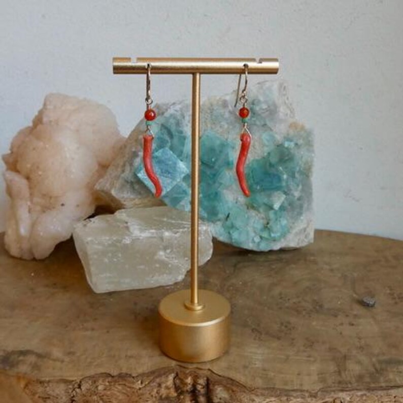 May include: A pair of dangle earrings featuring curved, bright orange-red horn-shaped charms suspended from silver-toned hooks. Each earring includes a small, round, translucent orange bead and a tiny turquoise-colored accent bead above the charm.