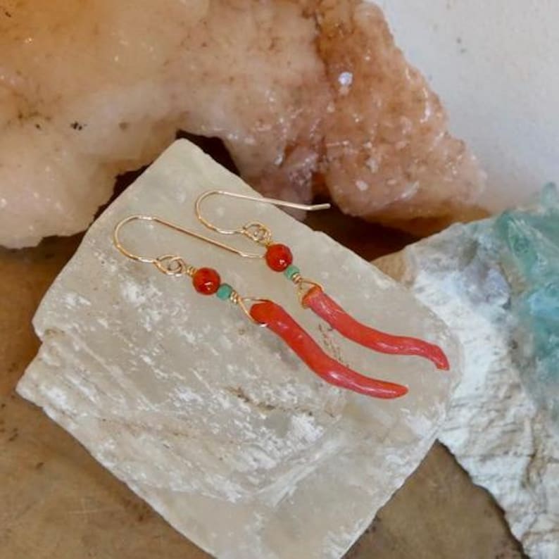 May include: A pair of gold-tone hook earrings featuring long, curved, coral-colored horn-shaped pendants. Each earring is accented with a small, round, faceted orange bead and a tiny, cylindrical, turquoise-colored bead attached to a gold wire.
