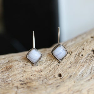 May include: A pair of silver drop earrings with a light blue agate stone in a square setting.