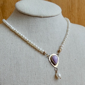 Puede incluir: Un delicado collar de perlas con un colgante dorado con una piedra en forma de l&aacute;grima de color p&uacute;rpura claro. Una sola perla cuelga de la parte inferior del colgante. El collar se exhibe en un maniqu&iacute;.