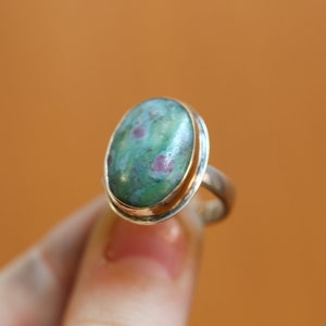 May include: A silver ring with a green and pink oval gemstone set in a gold bezel.