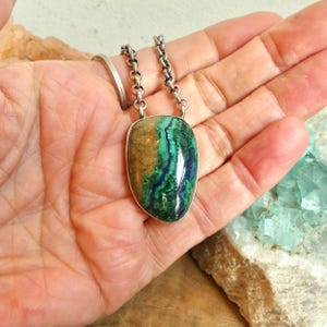 May include: A pendant necklace featuring a polished, teardrop-shaped azurite-malachite gemstone with swirling patterns of deep blue, vibrant green, and earthy brown, set in a silver-toned metal frame and attached to a thick, textured silver-toned chain.