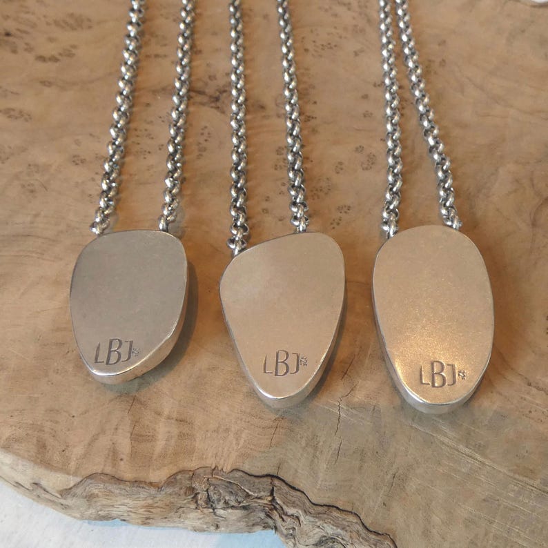 May include: Three silver necklaces featuring smooth, irregular, pebble-shaped pendants suspended from thick, round link chains. Each pendant is stamped with the letters LBJ and the number 925, indicating sterling silver composition.