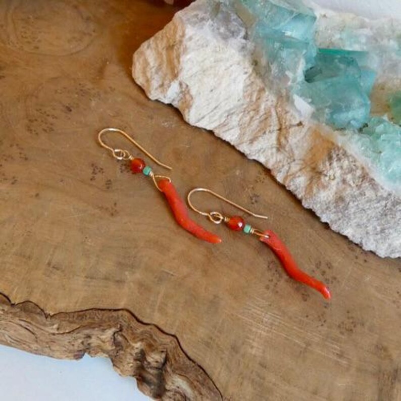 May include: A pair of gold-toned dangle earrings featuring a curved, branch-like red coral-colored element, a small round orange bead, and a tiny turquoise-colored accent bead suspended from a simple gold-toned wire hook for pierced ears.