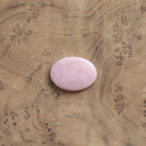 K&ouml;nnte beinhalten: Ein glatter, oval geformter rosa Edelstein mit polierter Oberfl&auml;che. Der Stein weist subtile Farbvariationen von blassem Blush bis hin zu zartem Ros&eacute; auf und hat eine gleichm&auml;&szlig;ige, abgerundete Silhouette, die einheitlich wirkt.