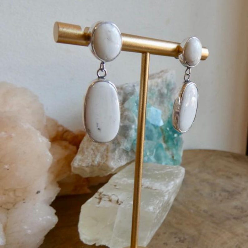 May include: A pair of drop earrings featuring smooth, oval-shaped white stones with subtle grey veining, set in polished silver-toned metal. Each earring consists of a smaller oval stud connected to a larger, dangling oval stone component.