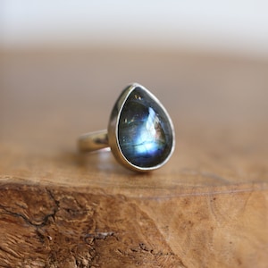 Puede incluir: Un anillo en forma de lágrima con una piedra preciosa de labradorita azul engastada en plata de ley.