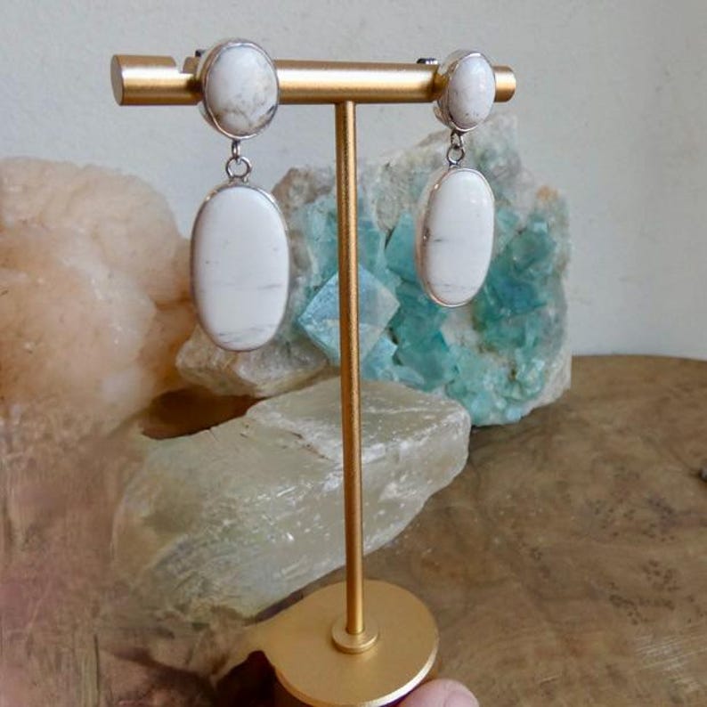 May include: A pair of drop earrings featuring smooth, oval-shaped white stones with subtle grey veining. Each earring consists of a smaller round stone at the top and a larger, elongated oval stone suspended below, set in polished silver-toned metal.