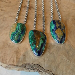 May include: Three necklaces featuring polished, irregular azurite-malachite cabochons set in silver-toned metal bezels. Each pendant hangs from a thick, silver-toned rolo chain, showcasing vibrant swirls of deep blue, bright green, and tan mineral patterns.