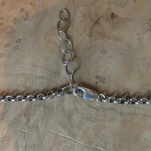 May include: A silver-toned metal chain necklace featuring a series of round interlocking links. The necklace includes a lobster claw clasp and an adjustable extender chain consisting of five larger oval links for varying the length of the piece.