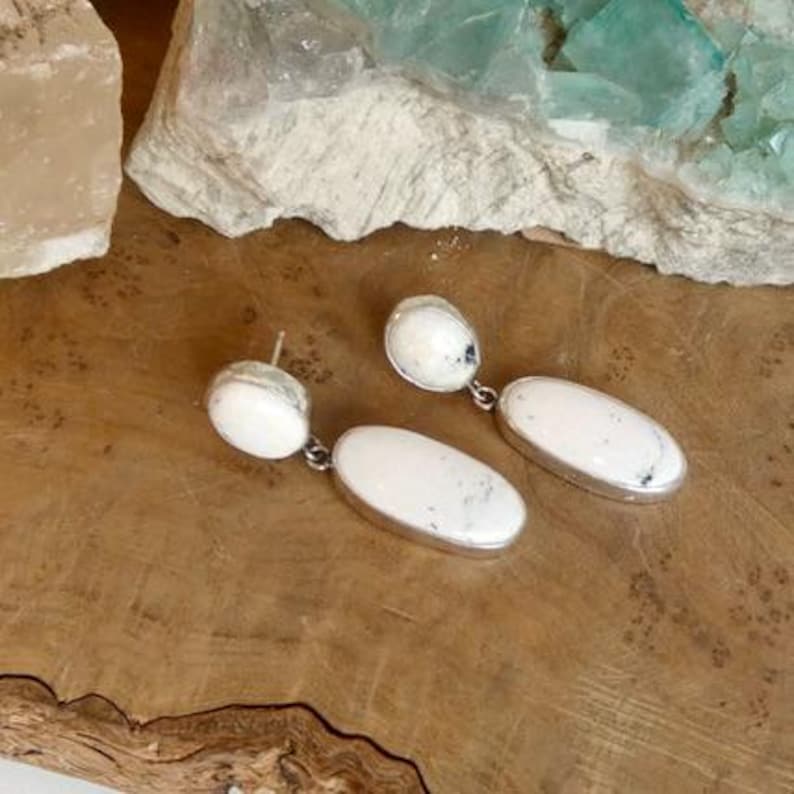 May include: A pair of drop earrings featuring two white oval stones with dark grey inclusions set in silver metal. Each earring consists of a smaller round top stone connected to a larger elongated oval bottom stone by a small silver link.