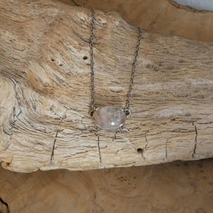 K&ouml;nnte beinhalten: Eine Halskette mit einem durchscheinenden, ovalen Steinanh&auml;nger in einer silberfarbenen Metallfassung mit Krappen. Der Anh&auml;nger h&auml;ngt an einer zarten, d&uuml;nnen silberfarbenen Metallkette mit kleinen, gleichm&auml;&szlig;igen Gliedern an beiden Seiten.