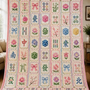May include: A rectangular quilt featuring a grid of embroidered tiles on a cream background. The tiles display colorful motifs including pink and purple flowers, blue and pink bows, green bamboo, dice, and various Chinese characters in blue and red.