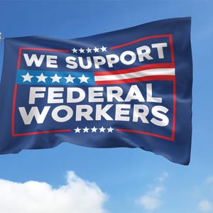 May include: A blue flag with white stars and red stripes, waving in the wind. The flag reads "WE SUPPORT FEDERAL WORKERS" in white text.