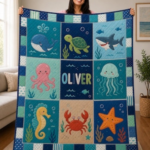 May include: A rectangular quilt featuring a grid of nine panels with illustrations of a blue whale, green sea turtle, shark, pink octopus, jellyfish, yellow seahorse, red crab, and orange starfish, with the name OLIVER in the center.