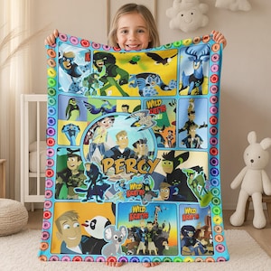 May include: A colorful Wild Kratts fleece blanket featuring cartoon characters and animals. The blanket has a blue border with donut-shaped designs. The blanket has the name "Percy" printed on it.