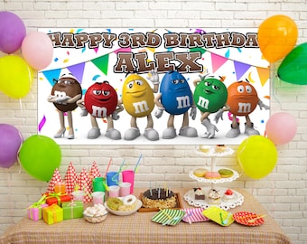 May include: A white banner with the text "Happy 3rd Birthday Alex" and colorful confetti.  The banner features six M&M's characters, including red, green, blue, yellow, brown, and orange.