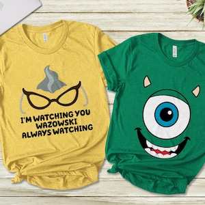 May include: Two t-shirts, one yellow with a gray and black image of a character with glasses and the text "I'm watching you Wazowski Always Watching", and the other green with a blue eye and a toothy grin.