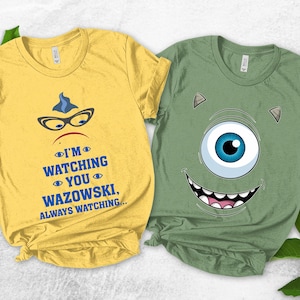 May include: Two short-sleeved t-shirts. One is yellow with a graphic of a character's face, glasses, and the text "I'M WATCHING YOU WAZOWSKI, ALWAYS WATCHING...". The other is green with a one-eyed monster face.