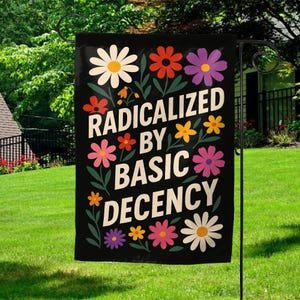 May include: Black garden flag with the text "RADICALIZED BY BASIC DECENCY" in white. The flag is decorated with colorful flowers in shades of red, orange, yellow, pink, purple, and white. The flag is hanging on a black metal stand in a grassy yard.