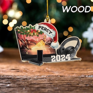 May include: Wooden Christmas ornament featuring a laptop with a dragon scene, a Santa hat with the name "Percy", and a pair of headphones. The ornament also includes the year "2024".