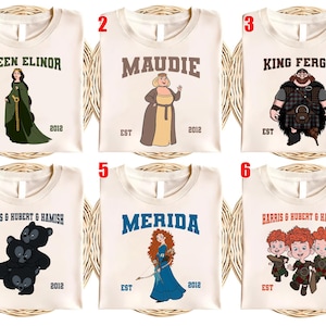 May include: Six cream-colored t-shirts with cartoon character designs. Each shirt features a different character name in bold letters, such as "Queen Elinor" or "Merida", along with the year "2012" and "EST".