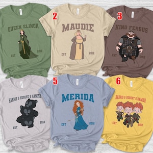 May include: A collection of six t-shirts featuring cartoon illustrations of characters from a movie. Each shirt has a different design, including characters like Queen Elinor, Maudie, King Fergus, Merida, and the triplets. The shirts are in various colors.