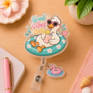 May include: A clear badge reel featuring a cartoon duck wearing heart-shaped sunglasses and floating on a turquoise inner tube. The text "Good Vibes Only" is above the duck. A small pink duck float charm hangs below.