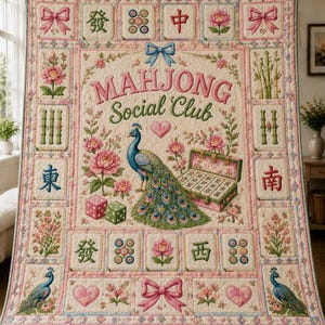 May include: A cream-colored quilt featuring the text "MAHJONG Social Club" in pink and green. The design includes a central peacock, a mahjong tile case, pink flowers, green dice, and borders decorated with bows, hearts, and mahjong tiles.