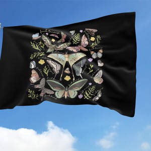 May include: Black flag with a colorful butterfly design. The flag features various butterfly illustrations in shades of green, pink, and white, along with floral accents and the text "fuck trump". The flag is waving against a blue sky.