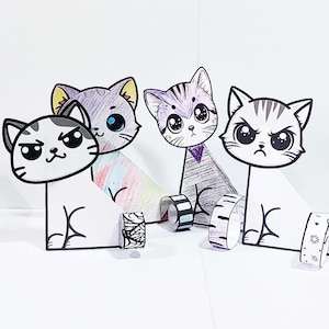 Op de afbeelding: Vier cartoon katfiguren met verschillende uitdrukkingen en kleuren. Elke kat heeft een andere kleur, waaronder grijs, paars en wit, met zwarte contouren. Decoratieve washi tape rollen staan voor elke kat.