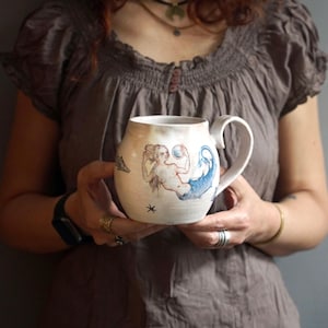 May include: A set of three ceramic mugs with a speckled, matte finish. The mugs are in shades of cream, light gray, and dark gray. Each mug has a simple, minimalist design, perfect for coffee or tea.