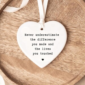 Può includere: Un ornamento in ceramica bianco a forma di cuore con il testo stampato in nero: Never underestimate the difference you made and the lives you touched, accompagnato da una piccola icona a forma di cuore nero e un nastro bianco per appenderlo.
