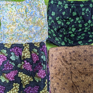 May include: Four fabric bowl cozies with different patterns. One has a floral design with yellow, blue, and white flowers. Another features green grape vines on a black background. The third has purple and green grapes. The last has a brown pattern.