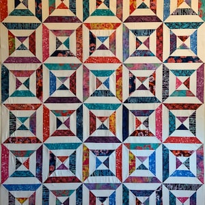 Puede incluir: Una colcha con un patrón geométrico de cuadrados y triángulos. La colcha está hecha de varias telas con diferentes colores y patrones, incluyendo rojo, azul, blanco y morado.