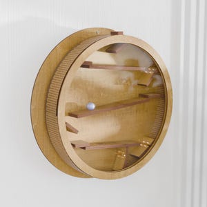 May include: A wooden marble run game mounted on a wall. The circular design features a clear front, wooden ramps, and a small marble. The outer ring has a textured design.