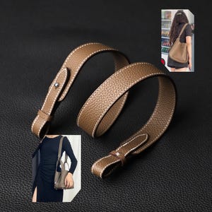 May include: A brown leather shoulder strap with white stitching. The strap is folded and laid flat on a brown surface.