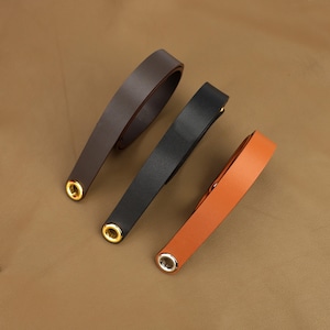 Puede incluir: Tres correas de cuero con ojales dorados. Las correas son marrón, negro y naranja.