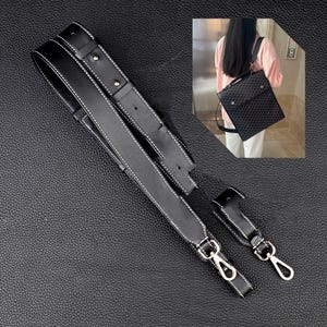 May include: Black leather adjustable shoulder strap with white stitching and silver hardware. The strap has two separate pieces that can be connected together with a buckle.