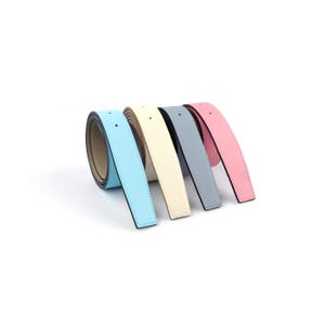 May include: A set of four leather belts in pastel colours, including light blue, cream, grey, and pink. Each belt features a textured, pebbled surface, smooth edges, and a single adjustment hole at the end of the strap, arranged in a row.