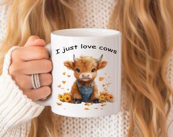 May include: White ceramic mug with a brown and white cartoon cow wearing blue overalls and surrounded by yellow sunflowers. The mug has the text "I just love cows" printed on it.
