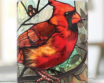 May include: A white ceramic mug with a stained glass design of a red cardinal perched on a branch. The cardinal's feathers are detailed with shades of red, orange, and yellow.