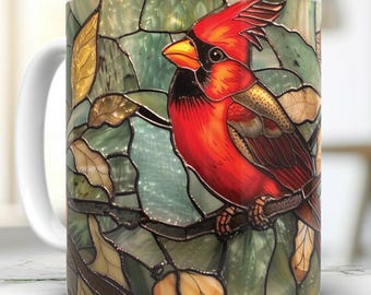 May include: A white ceramic mug with a stained glass design featuring a red cardinal perched on a branch. The cardinal has a black eye and a yellow beak.