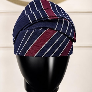 Peut inclure: Un chapeau bleu marine &agrave; rayures blanches et bordeaux. Le chapeau est pr&eacute;sent&eacute; sur une t&ecirc;te de mannequin noire. Le design du chapeau pr&eacute;sente une s&eacute;rie de rayures blanches verticales alternant avec des rayures bleu marine et bordeaux.