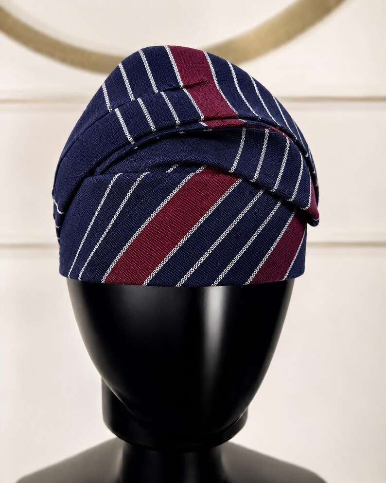 Peut inclure: Un chapeau bleu marine &agrave; rayures blanches et bordeaux. Le chapeau est pr&eacute;sent&eacute; sur une t&ecirc;te de mannequin noire. Le design du chapeau pr&eacute;sente une s&eacute;rie de rayures blanches verticales alternant avec des rayures bleu marine et bordeaux.
