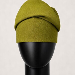 Peut inclure: Un chapeau vert chartreuse avec un design pli&eacute;, pr&eacute;sent&eacute; sur une t&ecirc;te de mannequin noire. Le chapeau a un tissu textur&eacute; et une forme arrondie, avec une bande autour de la base. Le fond est blanc cass&eacute; uni.